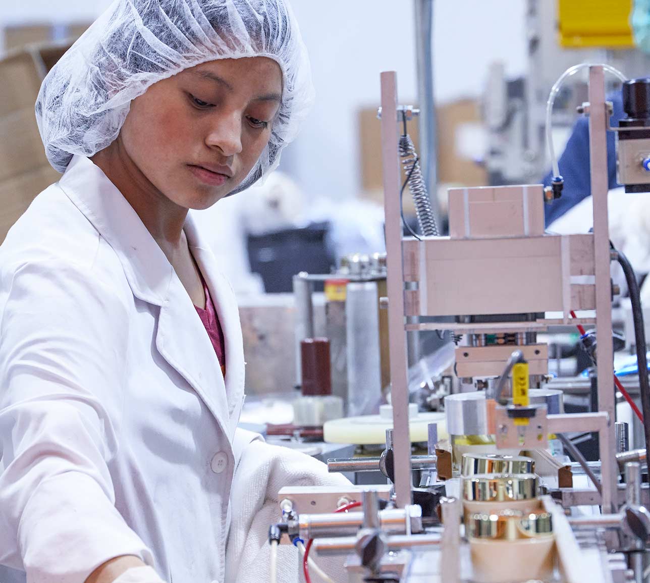 Worker assembling cosmetic containers on production line.