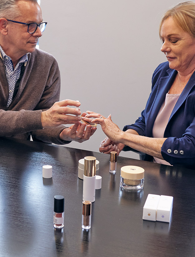 Two colleagues testing cosmetic products together at a table with skincare samples and packaging.