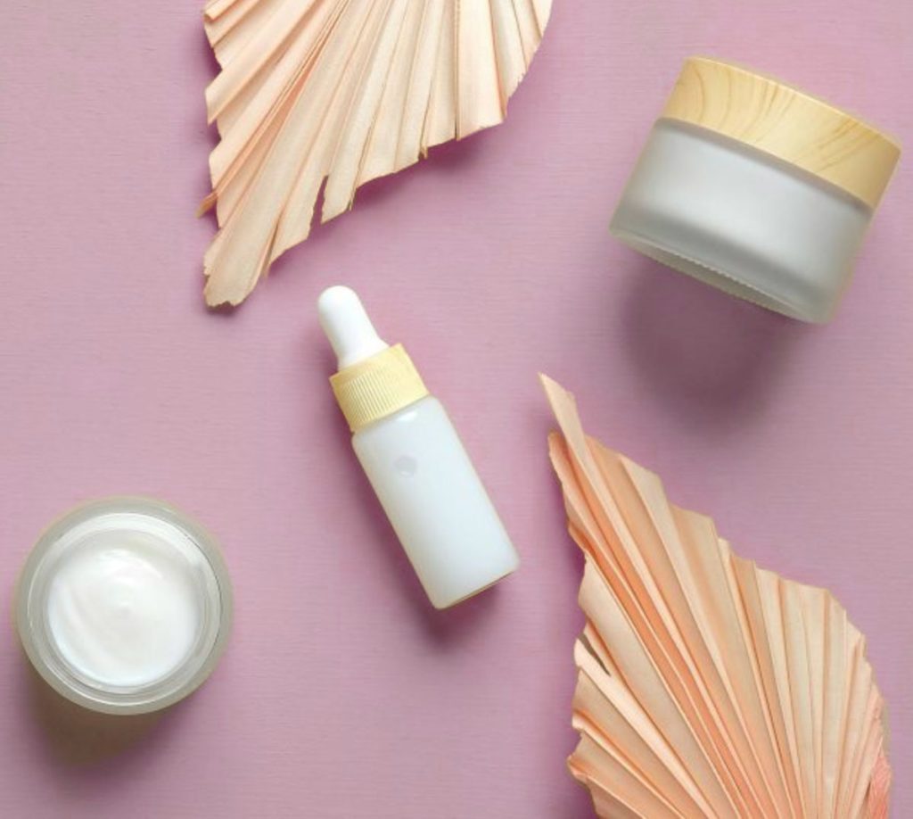 Minimal skincare products arranged on soft purple background with cream jar and serum bottle.