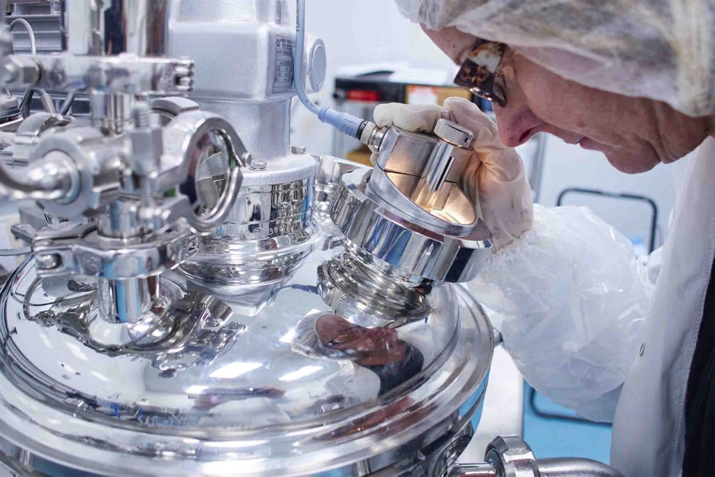Scientist closely inspecting stainless steel processing equipment inside a controlled laboratory setting.